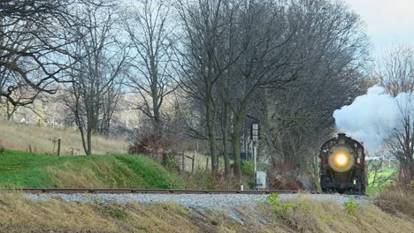 a view of a steam passenger train approaching from a long distance on a cold fall day with lots of smoke