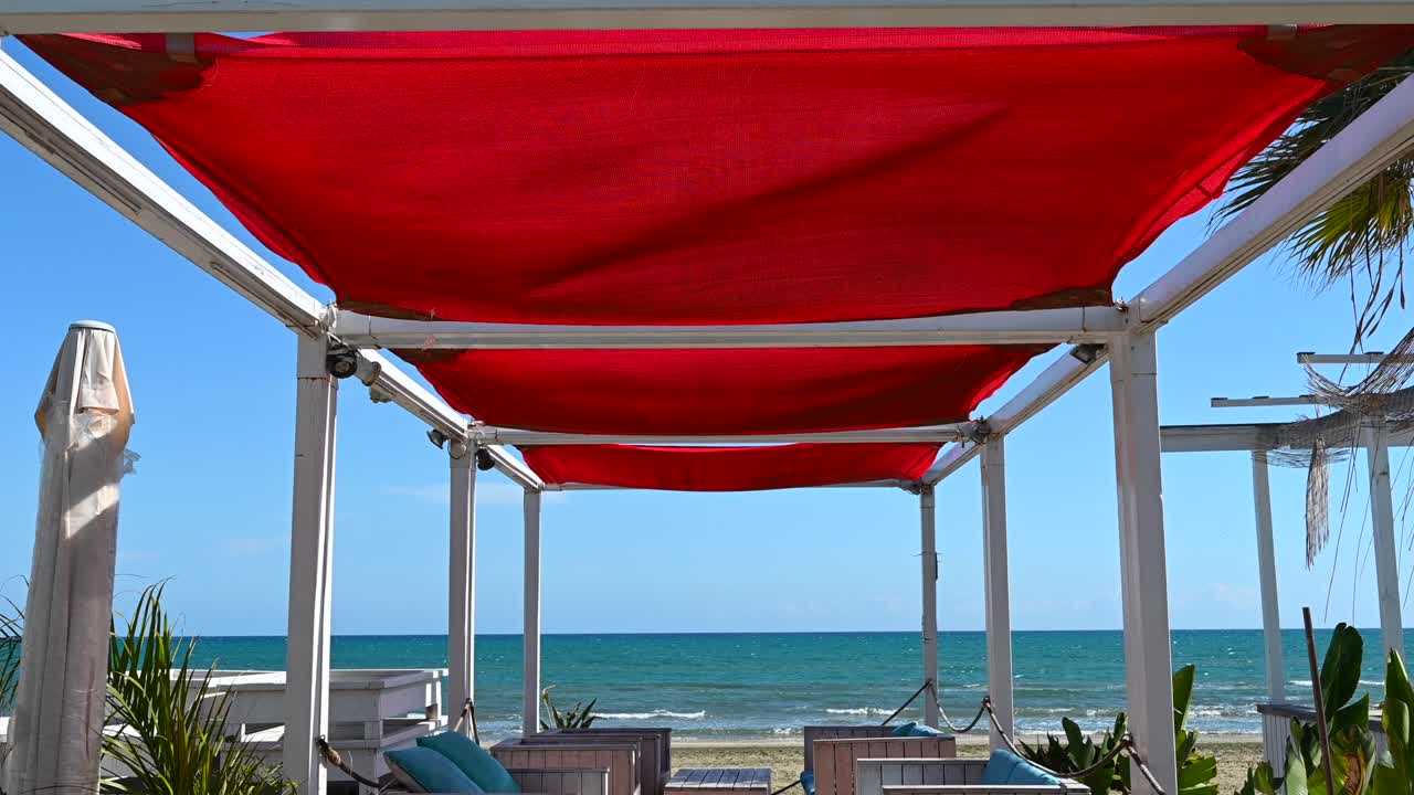A seaside lounge shaded by a striking red canopy, overlooking the Mediterranean Sea in Larnaca, Cyprus