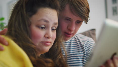 young downs syndrome couple sitting on sofa watching digital tablet at home