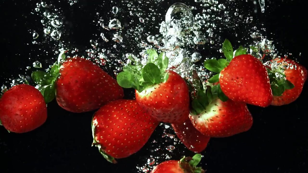 Fragole rosse fresche che cadono nell'acqua con bolle su sfondo nero
