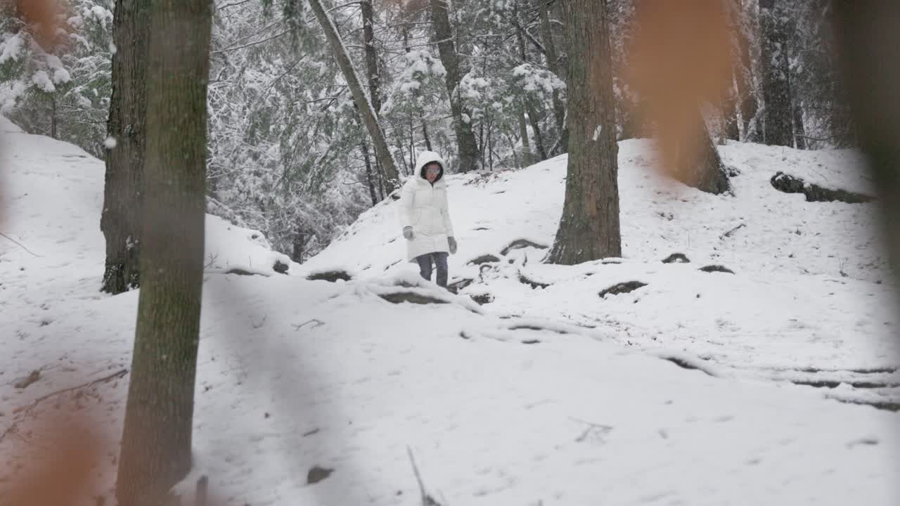 Hiker Woman in long warm jacket walking down a Winter forest path during a snow storm pauses to contemplate (4K)