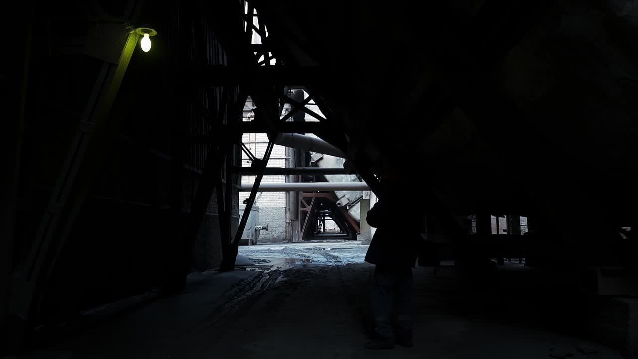 Silhouette of a male worker in a helmet walking through the territory of an industrial enterprise. Old coal power plant. Black tunnel