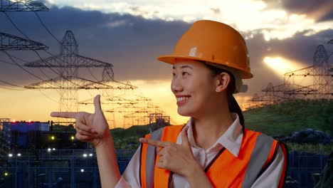 close up of asian female engineer with safety helmet smiling and pointing to side while standing near high voltage tower