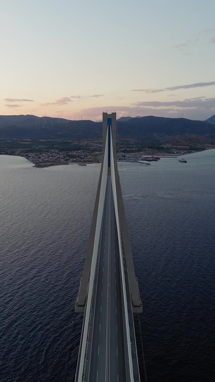 Ripresa statica verticale con drone direttamente sopra il Ponte Rio-Antirrio al tramonto. Veicoli che attraversano il ponte sottostante. Luce dorata serale. Filmati aerei di infrastrutture greche.