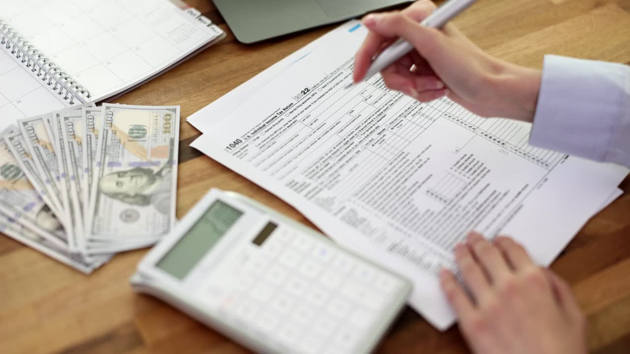 Woman is handwriting us 1040 tax form and using calculator