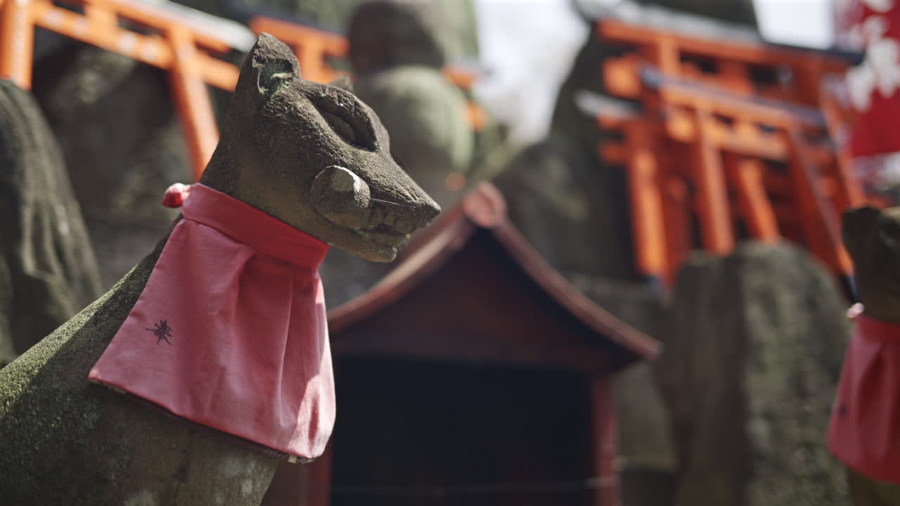 Stone fox statues adorned with red scarves at a beautiful shrine in Japan. This site showcases traditional architecture within a serene environment. Kyoto, Japan, Fushimi Inari