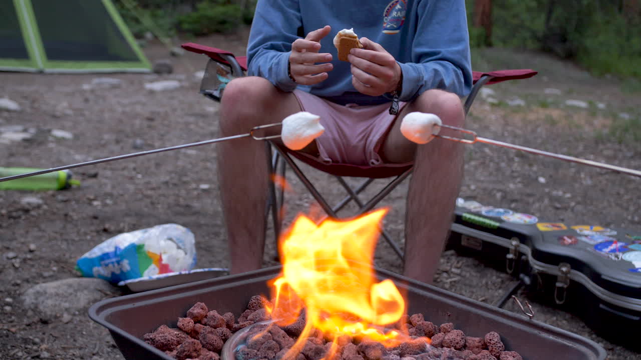 eating smores by the fire camping while toasting marshmallows