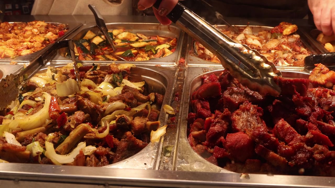 Persone che prendono cibo da un buffet cinese, mani in primo piano.