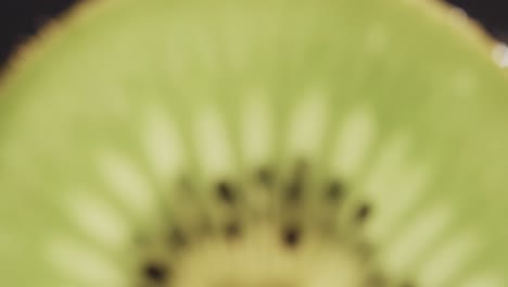 Micro-video-of-close-up-of-kiwi-fruit-slice-with-copy-space-on-black-background