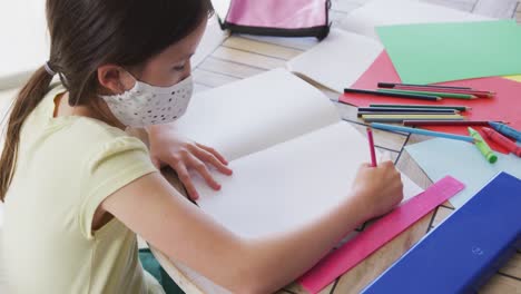 girl wearing face mask doing homework at home