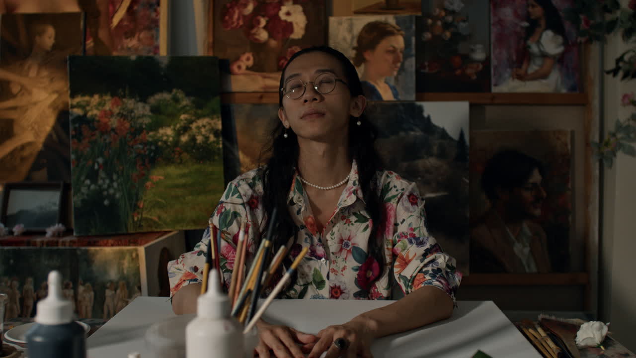 Artist in studio paints with focus amid diverse artworks