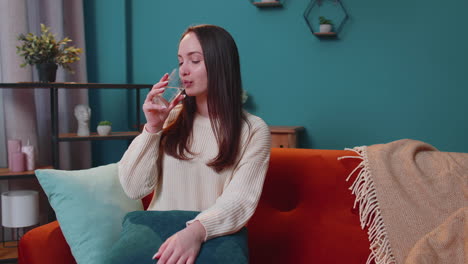 sedienta una mujer joven sentada en casa sosteniendo un vaso de agua natural hacer sorbos bebiendo agua tranquila