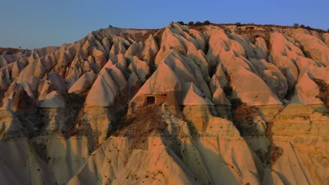 Rock-cut-cave-house-in-Cappadocia-landscape-during-sunset,-pull-back-aerial
