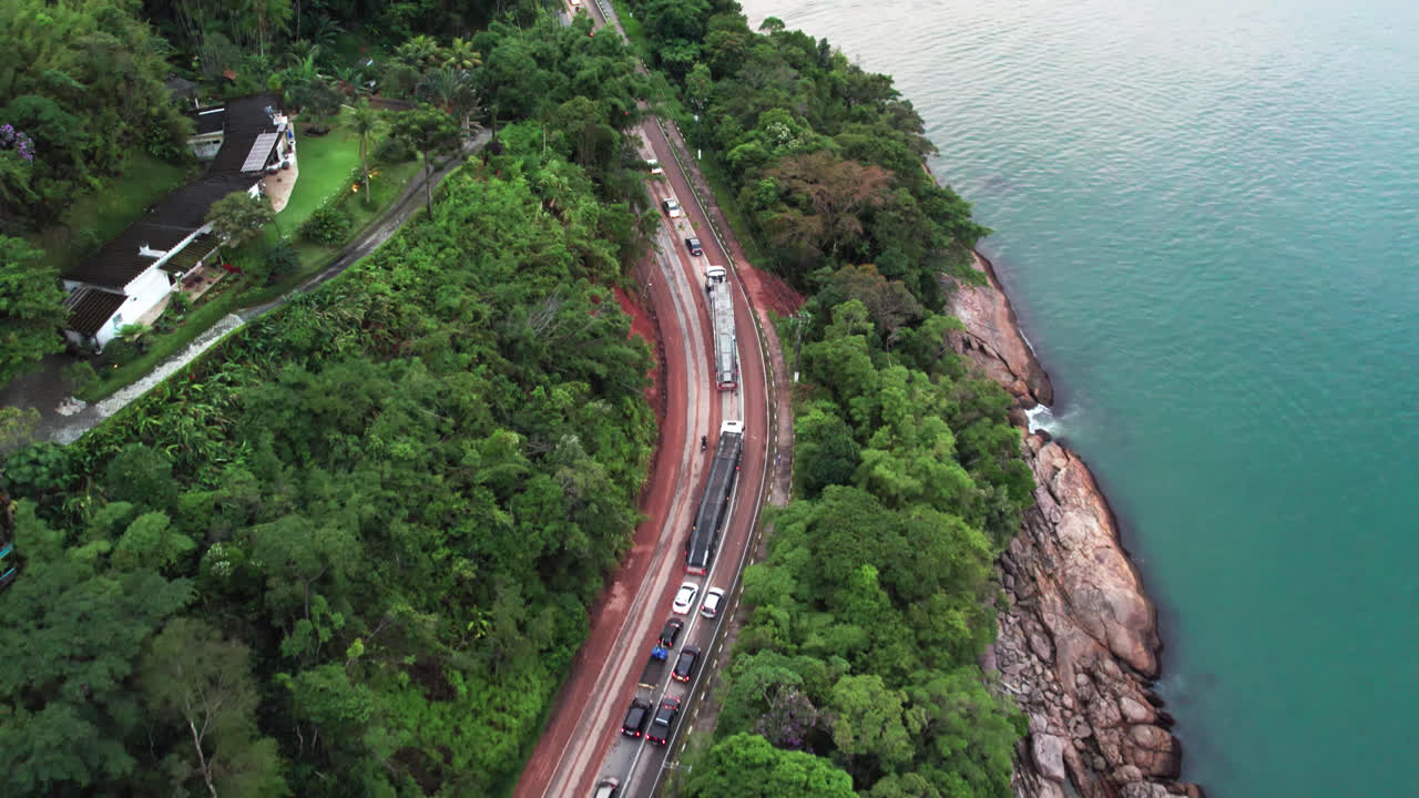 Traffic stopped on way down to beach, Ubatuba, Brazil. Aerial forward showing the beautiful coastal road with blue and green sea water with rocks