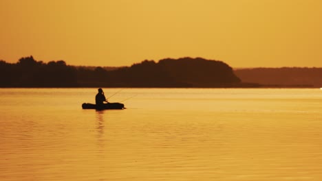 golden sunset and the silhouette of a man throwing a fishing rod from the boat. fisherman is catching fish from a rowboat in the evening on the background of natural landscape.