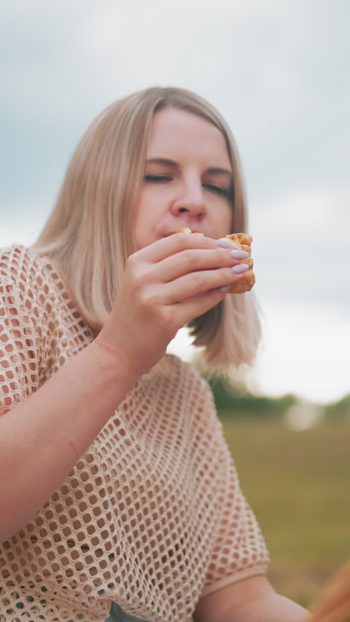 joven adulto disfruta de la pastelería mientras los niños se sientan cerca, centrados en algo, canasta de picnic en medio de un vasto fondo de campo de granja creando un momento familiar al aire libre pacífico