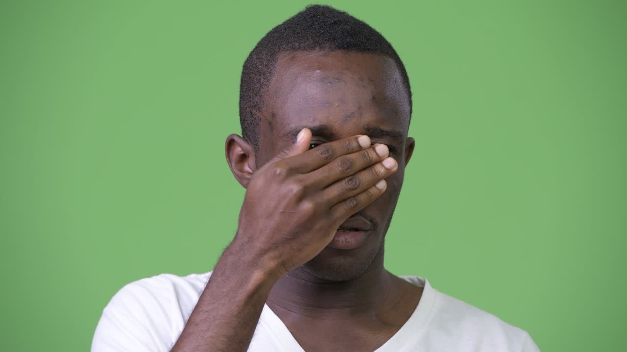 Giovane uomo africano che si copre gli occhi per non voler vedere qualcosa