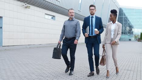 african american businesswoman and two caucasian businessmen talking and walking down the street