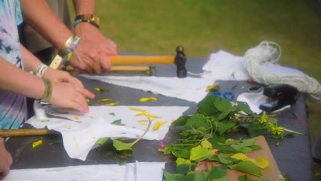 cerrar las manos de un niño y adultos colocando diferentes hojas y flores en un trozo de tela para golpearlo con un martillo para crear imágenes interesantes actividad familiar parque infantil para niños