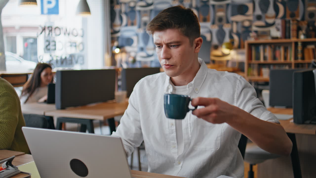 Impiegato che beve caffè in un coworking, primo piano. Uomo concentrato che fissa il portatile