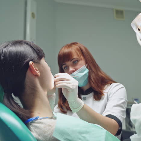 Red-haired female dentist looking at patient's teeth before treating them in stomatology office. Dentist treating teeth of woman patient.