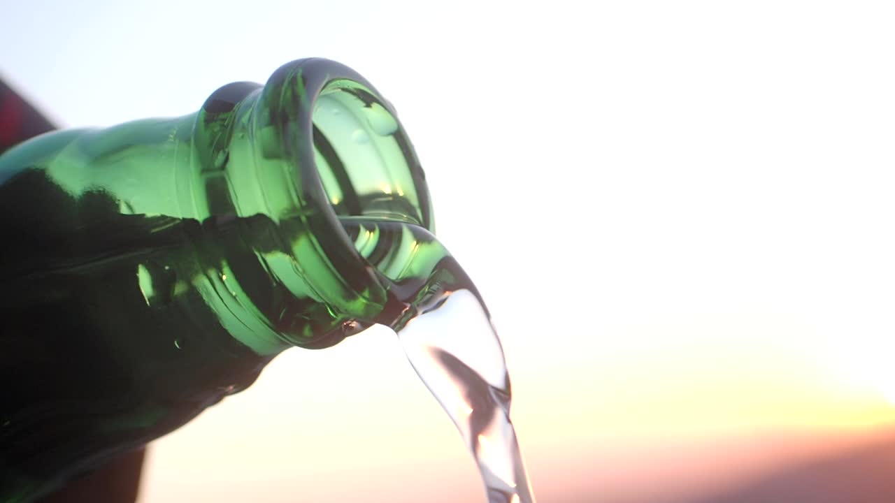 Water pouring from a green glass bottle at sunset