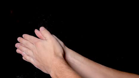 an athlete preparing for workout by rubbing, chalking and clapping his hands for evenly distributing the chalk powder, isolated on black background