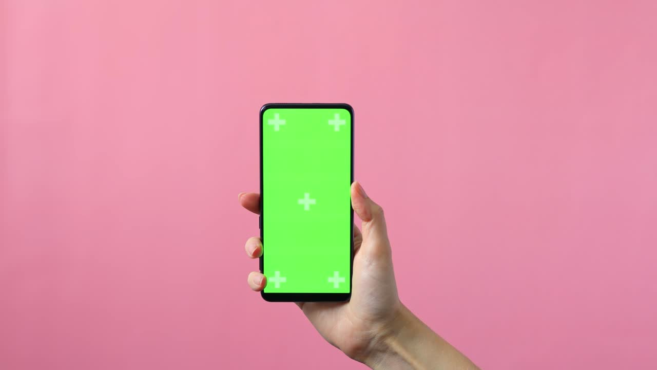 primer plano de manos femeninas sosteniendo un teléfono inteligente con una pantalla verde en blanco que muestra espacio de copia para el diseño de aplicaciones o sitios web, en fondo rosa, maqueta.