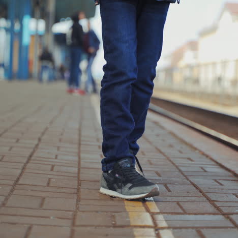 little boy is standing on the railway station and waiting for the passenger train. alone boy going forward and backward on the platform. close-up