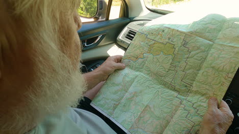 closeup of senior man looking at folded out map, sitting in driver seat of car