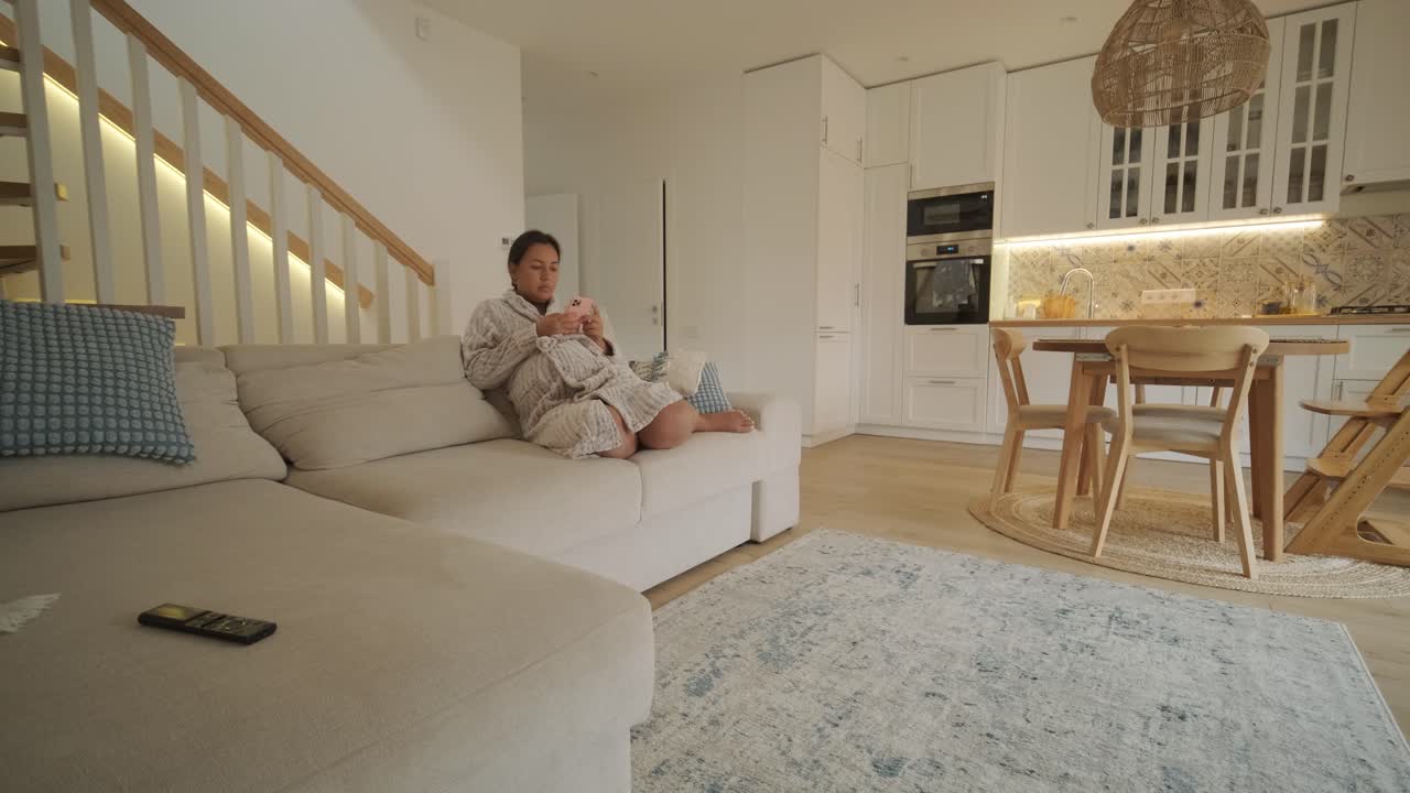 Evde rahatça oturmuş, bir televizyon konsolunda video oyunlarının tadını çıkaran güzel bir hamile kadın. Sahne, rahat bir ortamda dinlenmeyi, modern eğlenceyi ve anneliği bir araya getiriyor