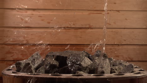 Water-splashing-over-hot-coals-in-sauna,-low-angle-close-up