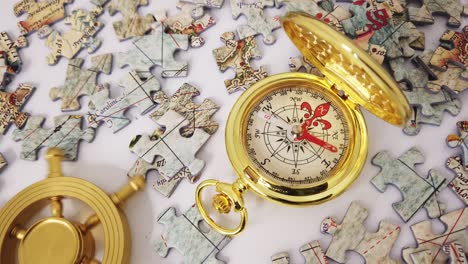 Golden-compass-pointing-for-directions-and-a-rudder-wheel-turned-left-and-right-with-jigsaw-puzzles-of-world-map-lying-around