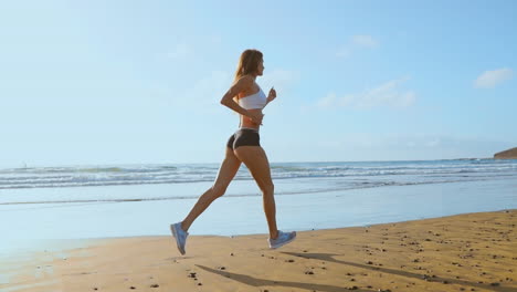 beautiful woman in sports shorts and t-shirt running on the beach with white sand and blue ocean water on the island in slow motion. waves and sand hills on the back won