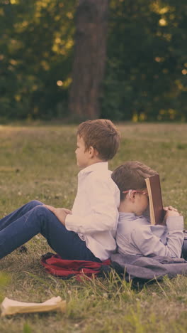 upset schoolboy throws textbook and friend tired of preparing for exam sleeps with book on face on green lawn in park