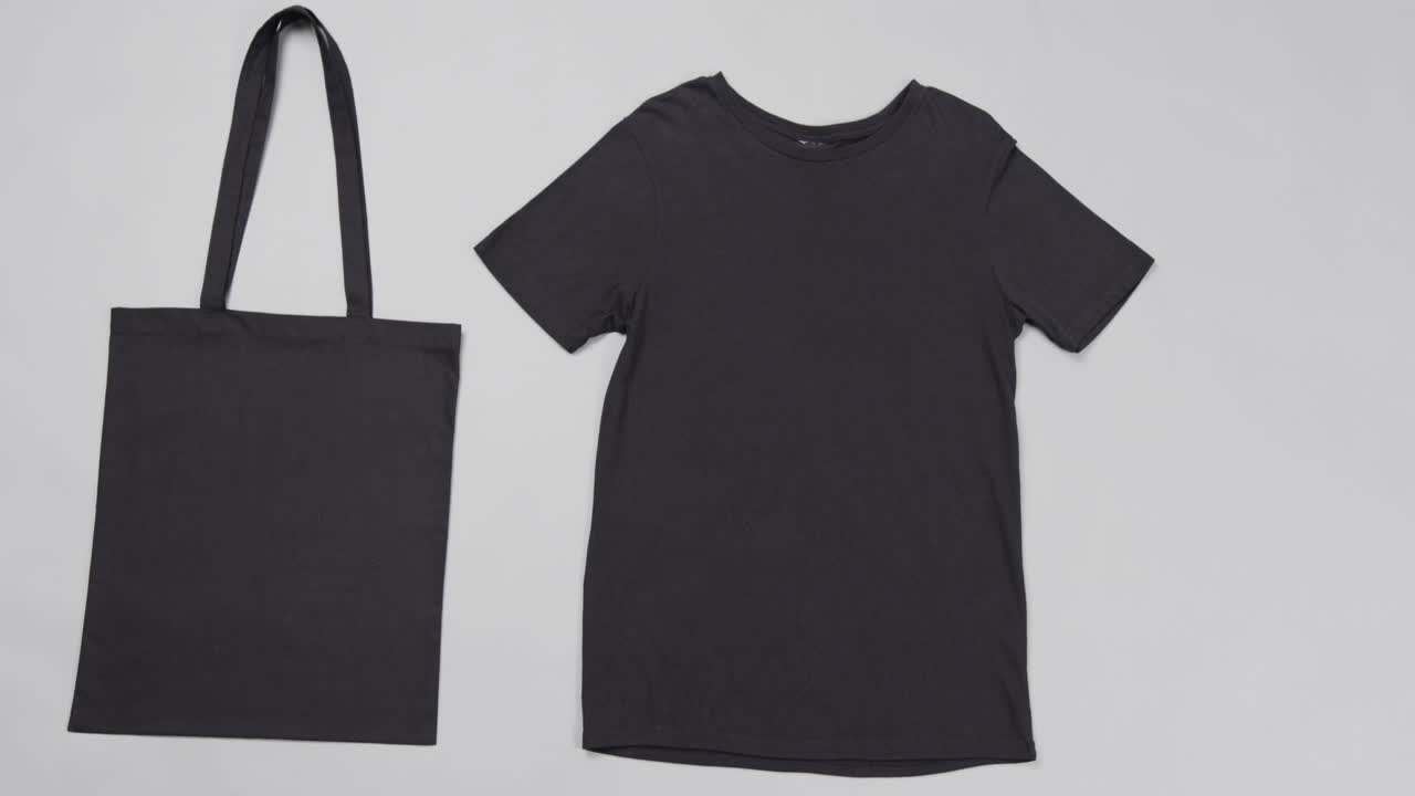 Close up of black bag and t-shirt on grey background, with copy space, slow motion