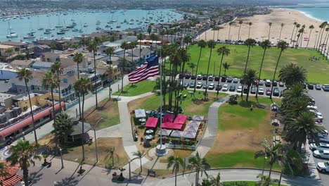 aerial view of an american flag blowing in the wind at peninsula park, in newport beach, california