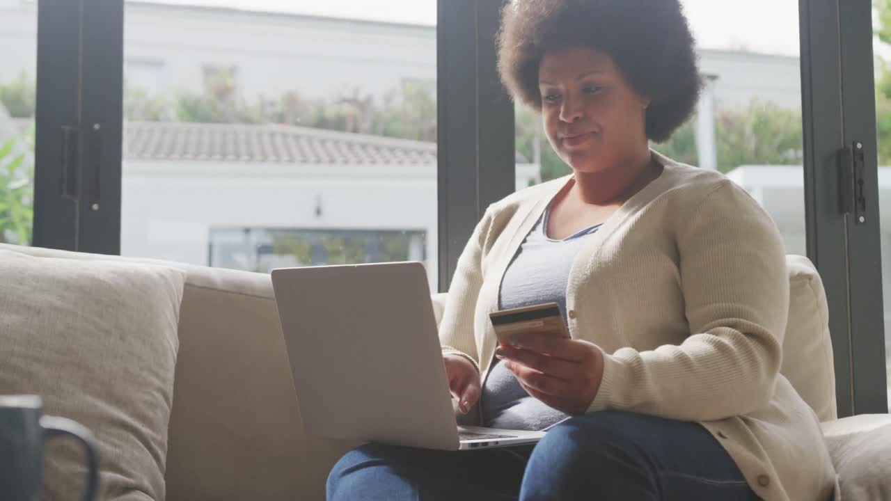 video de una feliz mujer afroamericana de tamaño plus con tarjeta de crédito y usando una computadora portátil