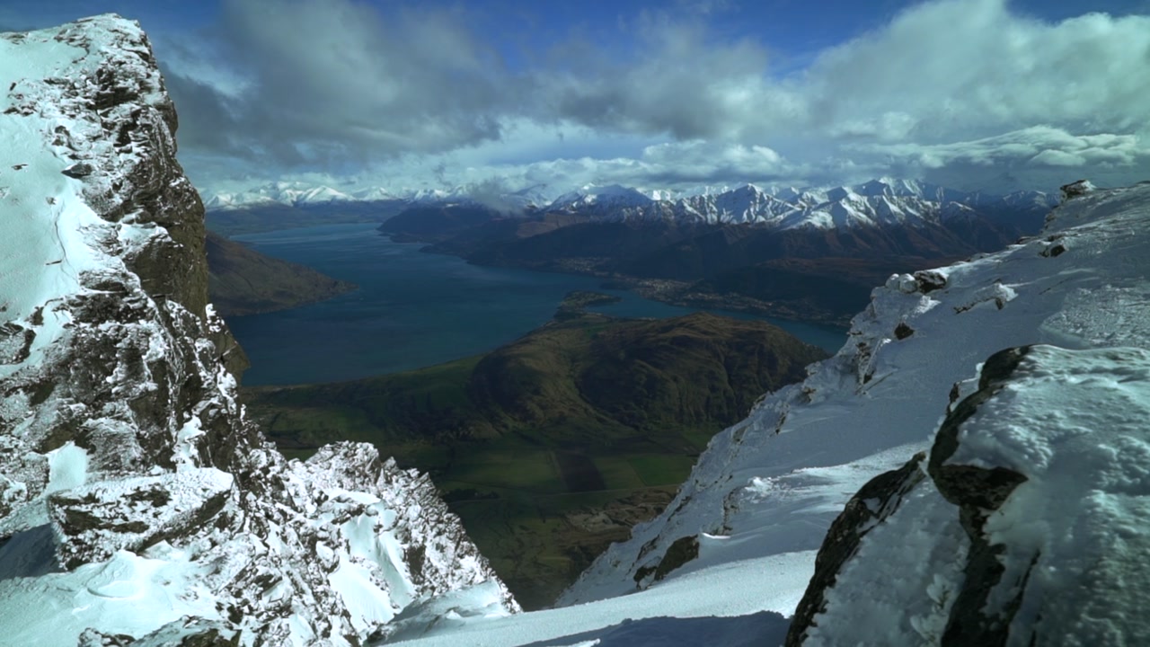 Look out The Remarkables Ski Resort jagged snowy covered peaks Rock face cold winter morning sunny blue sky clouds New Zealand Lake Wakatipu Queenstown Frankton lush green valley blowing snow slide