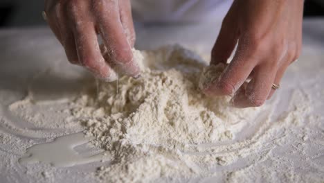 Close-Up-view-of-female-hands-mixing-flour-with-eggs-and-milk-on-the-kitchen-surface.-Slow-motion-shot