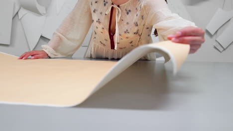 young female designer with tape-line on her neck standing in dressmaking studio and drawing lines with chalk and rule. female couturier in atelier cutting out a pattern for future clothes.