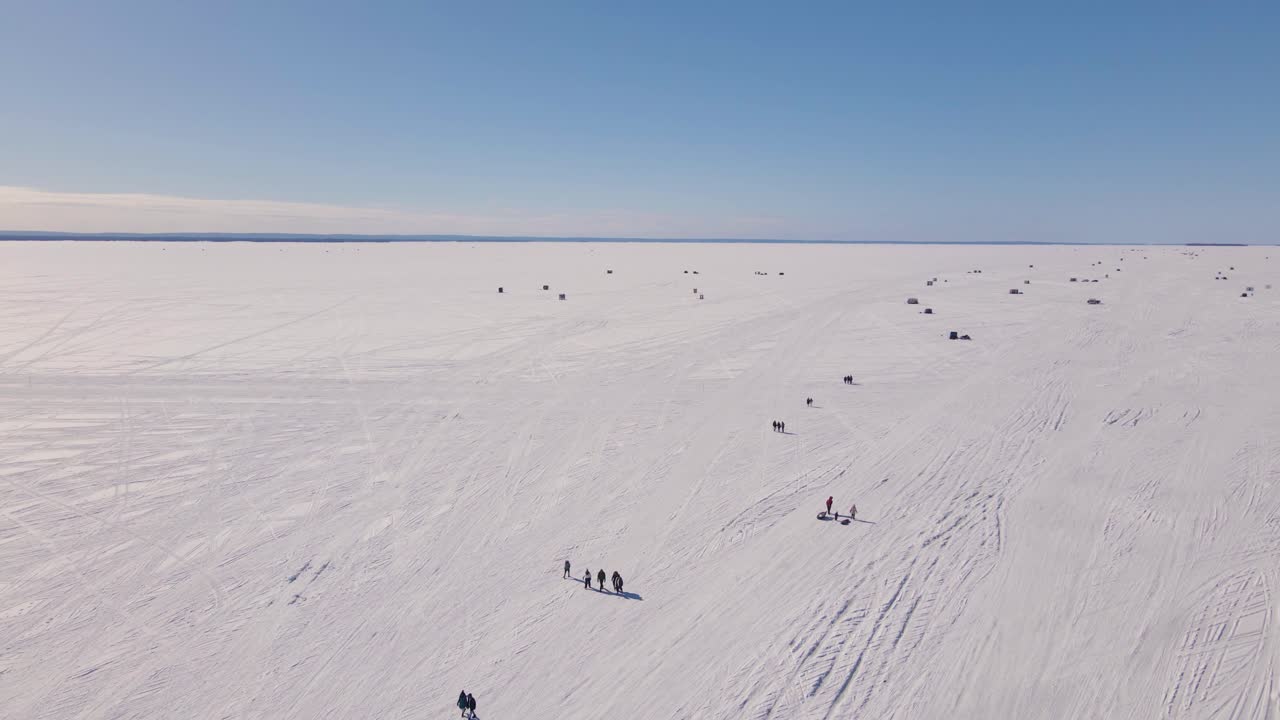 un drone de gran ángulo que sigue a la familia y amigos caminando por un lago congelado de vuelta a la orilla después de un largo día de pesca en el hielo durante un hermoso día de invierno frío y soleado en una parte remota de canadá