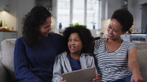 Smiling-mixed-race-lesbian-couple-and-daughter-using-digital-tablet-on-couch