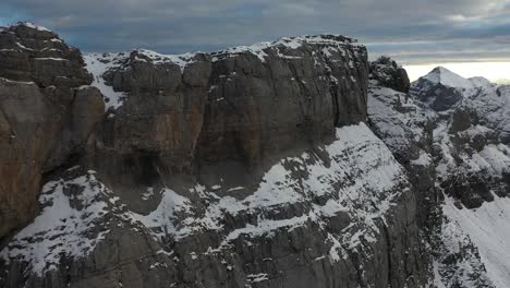 Drone-shot-moving-forwards-next-to-a-steep-cliff-side-with-bare-rocks,-snow-and-ice