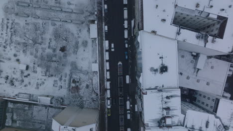 Aerial-birds-eye-overhead-top-down-view-of-tram-passing-around-vehicles-in-street.-Snowed-roofs-in-winter-city.-Berlin,-Germany