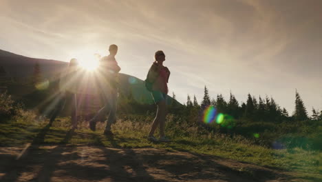 a group of friends with backpacks rises up the mountain in the rays of the setting sun active lifest