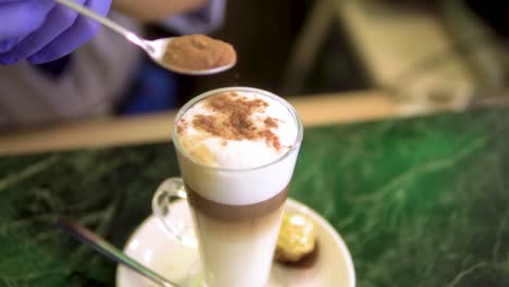 barista cerca de preparar café con leche de autor espolvoreando chocolate en la parte superior con guantes morados a cámara lenta