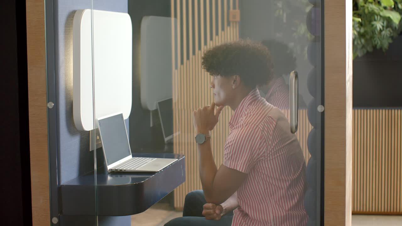 Uomo che usa il laptop in una cabina privata per concentrarsi, lavorando in un ufficio moderno.