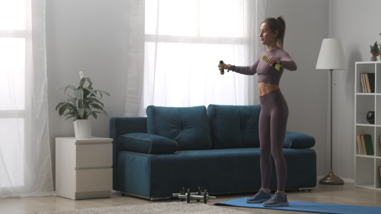 deporte y fitness en casa mujer joven está entrenando con pesas de pie en la sala de estar de su apartamento moderno mujer deportiva en el interior