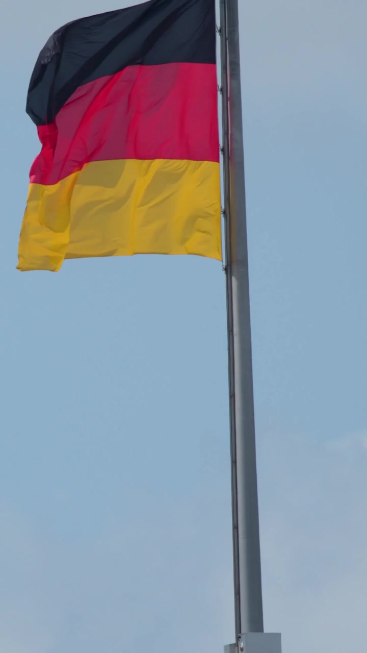 Una bandiera nazionale tedesca sventola su un'asta d'argento contro uno sfondo di cielo coperto.